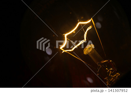 glowing star filament incandescent light bulb illuminated against a dark background. The warm light and vintage filament design create dramatic visual representing innovation, creativity, inspiration 141307952