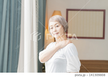 リビングの窓辺で朝のストレッチヲするシニア女性 リビングの窓辺で朝のストレッチヲするシニア女性 141309808