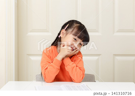 Cheerful young girl playing with a pencil behind her ear and smiling brightly. Cheerful young girl playing with a pencil behind her ear and smiling brightly. 141310716
