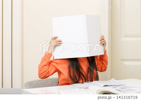Shy or playful child completely hiding her face behind a large open white book. Shy or playful child completely hiding her face behind a large open white book. 141310719