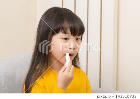 Asian little girl applying lip balm dry lips skincare child healthcare concept 141310738