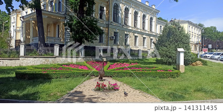 Beautiful flower bed shaped like a peacock tail in a park near a historic building Beautiful flower bed shaped like a peacock tail in a park near a historic building 141311435