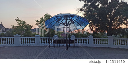 Cozy park terrace with large umbrella shaped canopy and benches at sunset 141311450