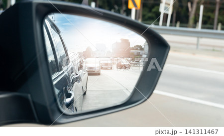 View through a car's side mirror. Focus on the side of the car. Showing other vehicles moving along a highway. Perspective captures the flow of traffic and the surroundings during a commute in city. 141311467
