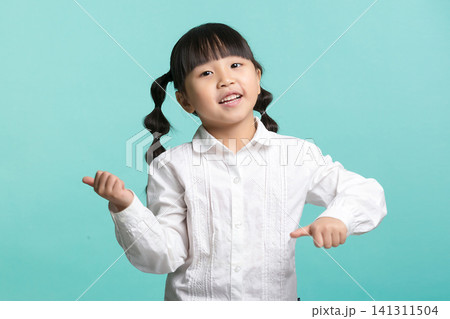 A cute little girl with braided pigtails pointing both thumbs to her side with an energetic and confident expression. 141311504
