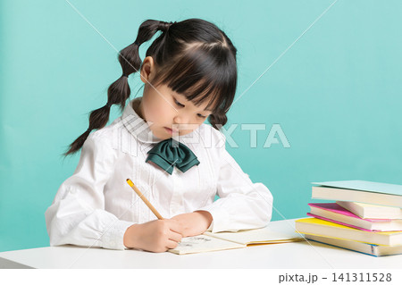 A diligent elementary school girl leaning over her desk and writing carefully in her notebook with a pencil. A diligent elementary school girl leaning over her desk and writing carefully in her notebook with a pencil. 141311528