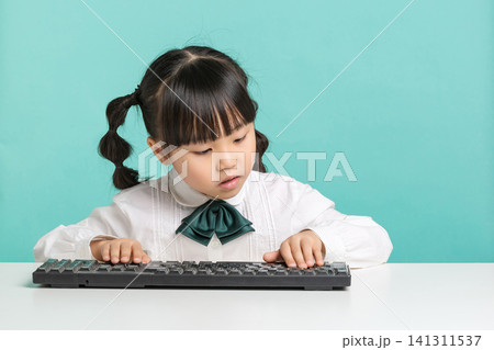 A focused elementary school student typing or practicing on a black computer keyboard placed on her white desk. A focused elementary school student typing or practicing on a black computer keyboard placed on her white desk. 141311537