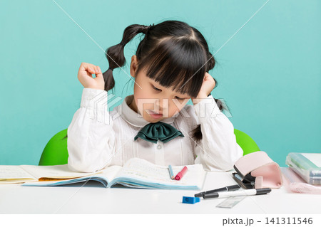 A stressed young girl resting her head on her hand while struggling with a difficult textbook assignment at her desk. A stressed young girl resting her head on her hand while struggling with a difficult textbook assignment at her desk. 141311546