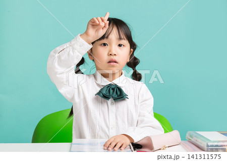 A curious young student pointing her finger upward to point out an idea or a question during a classroom lesson. A curious young student pointing her finger upward to point out an idea or a question during a classroom lesson. 141311575