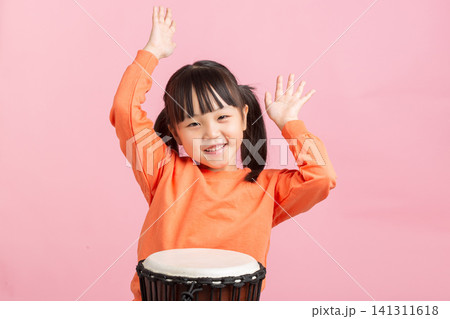 Happy young girl raising her hands and smiling behind an African djembe drum in studio. Happy young girl raising her hands and smiling behind an African djembe drum in studio. 141311618