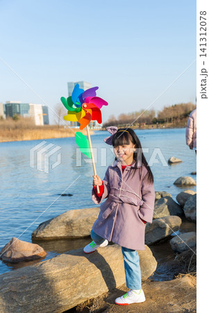 a happy little girl stands on a riverside rock, holding a colorful pinwheel. a happy little girl stands on a riverside rock, holding a colorful pinwheel. 141312078