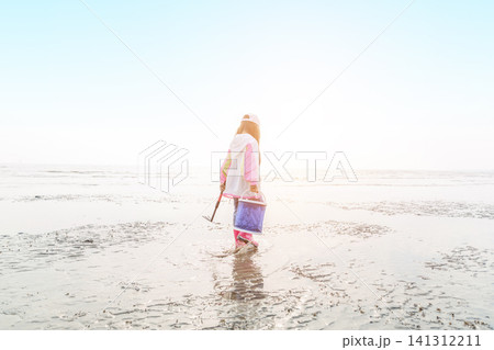 Full length of a young girl holding a blue bucket and walking on a vast mudflat at low tide. Full length of a young girl holding a blue bucket and walking on a vast mudflat at low tide. 141312211