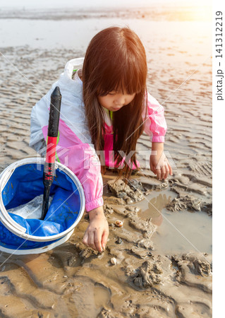 Little girl sitting on her heels on a mudflat, holding mud in her hands with a blue net nearby. Little girl sitting on her heels on a mudflat, holding mud in her hands with a blue net nearby. 141312219