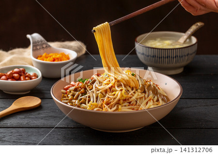 lifting rich sesame noodles with chopsticks from a bowl, authentic Wuhan hot dry noodles close-up. 141312706