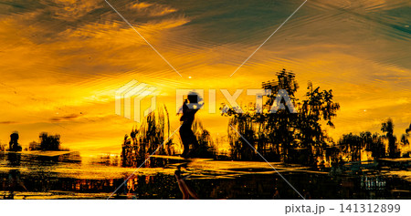Silhouette of a girl standing by reflective water surface at dramatic golden orange sunset, nature and travel concept Silhouette of a girl standing by reflective water surface at dramatic golden orange sunset, nature and travel concept 141312899