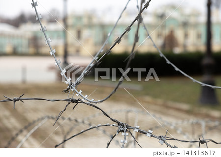 Sharp coiled razor wire creates a physical barrier before an ornate historical building, symbolizing strict restriction, protection, geopolitical conflict, or deep civic tension today Sharp coiled razor wire creates a physical barrier before an ornate historical building, symbolizing strict restriction, protection, geopolitical conflict, or deep civic tension today 141313617