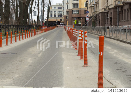 Orange reflective traffic delineators line a city street, effectively separating vehicle lanes to enhance road safety and manage efficient urban transport flow for local commuters Orange reflective traffic delineators line a city street, effectively separating vehicle lanes to enhance road safety and manage efficient urban transport flow for local commuters 141313633