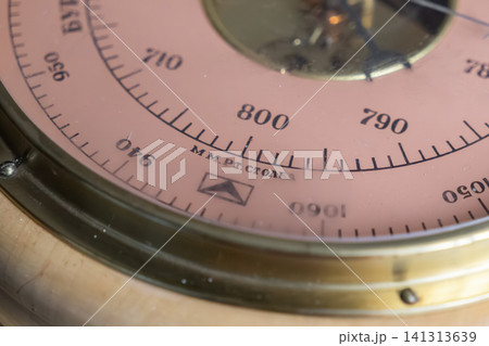 A detailed macro view of an antique brass barometer gauge featuring a circular scale and needle, highlighting scientific meteorological tools used for tracking atmospheric pressure A detailed macro view of an antique brass barometer gauge featuring a circular scale and needle, highlighting scientific meteorological tools used for tracking atmospheric pressure 141313639