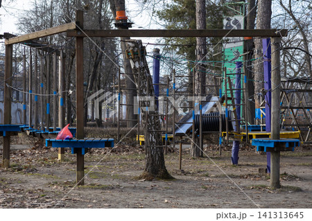 A rope park obstacle course with wooden platforms and hanging bridges in an autumn forest, offering adventure and recreational activity for outdoor exercise in a public city park 141313645