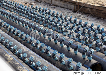 A series of black plastic irrigation pipes with light blue fittings aligned on a construction site, illustrating modern agricultural water management and efficient field infrastructure 141313646