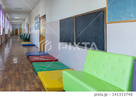 Empty school hallway with colorful floor mats and lime green chairs placed along the wall for student seating areas, showcasing a bright educational environment for children today Empty school hallway with colorful floor mats and lime green chairs placed along the wall for student seating areas, showcasing a bright educational environment for children today 141313748