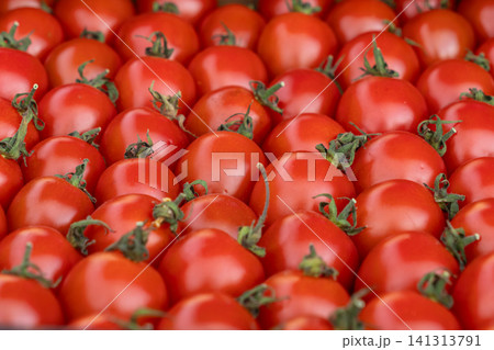Fresh red cherry tomatoes arranged in a dense pattern covering the frame, highlighting vibrant skin texture and natural stems for a healthy organic food concept in culinary arts 141313791