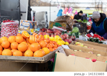 Fresh oranges and assorted produce displayed on a wooden table at an outdoor street market, highlighting local harvest commerce and seasonal nutrition in a busy retail setting 141313803