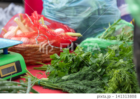 Fresh bundles of green parsley and dill sit beside a small electronic scale and a wicker basket of garlic at a vibrant outdoor farmers market stall for healthy culinary cooking 141313808