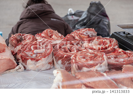 Fresh raw beef rolls displayed on a butcher market table with a seller in the background, capturing a rustic culinary scene for grocery retail, gourmet food preparation and supply 141313833