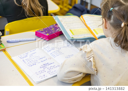 A young primary school student writes in a math notebook at a wooden desk, capturing a moment of focus and academic progress during a classroom lesson in an elementary school A young primary school student writes in a math notebook at a wooden desk, capturing a moment of focus and academic progress during a classroom lesson in an elementary school 141313882