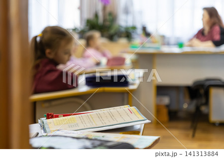 Schoolchildren sit at desks in a bright classroom while an adult teacher instructs, capturing a focused and educational atmosphere during a primary school lesson for young students 141313884