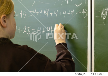 A diligent schoolchild writes complex math equations on a green chalkboard in an elementary classroom, showing academic focus and steady learning progress during a primary lesson A diligent schoolchild writes complex math equations on a green chalkboard in an elementary classroom, showing academic focus and steady learning progress during a primary lesson 141313896