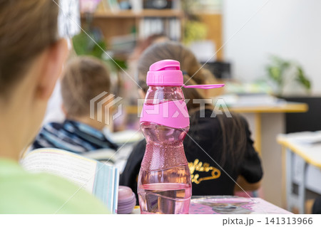 A pink reusable water bottle sits on a classroom desk near elementary students during a lesson to promote hydration and health in a focused academic environment for young kids 141313966