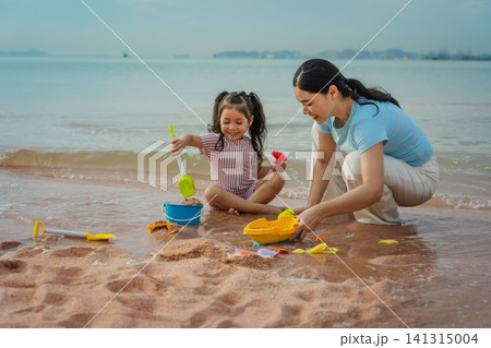 happy preschool child girl playing sand toy with mother on sea beach in Pattaya, Thailand happy preschool child girl playing sand toy with mother on sea beach in Pattaya, Thailand 141315004