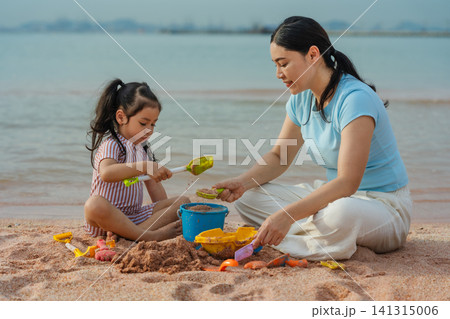 happy preschool child girl playing sand toy with mother on sea beach in Pattaya, Thailand 141315006