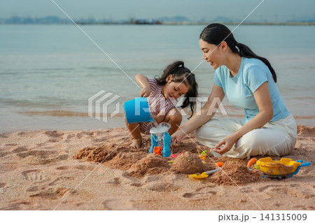 happy preschool child girl playing sand toy with mother on sea beach in Pattaya, Thailand 141315009
