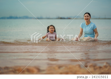 happy preschool child girl playing water splashing with her mother on sea beach in Pattaya, Thailand happy preschool child girl playing water splashing with her mother on sea beach in Pattaya, Thailand 141315011