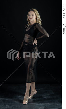 Young blonde dancer wearing transparent black dress and high heels posing in studio with black background Young blonde dancer wearing transparent black dress and high heels posing in studio with black background 141315168