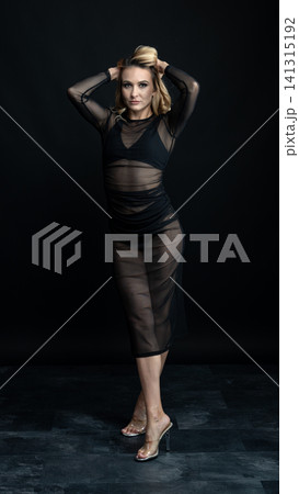 Young blonde dancer wearing transparent black dress and high heels posing in studio with black background Young blonde dancer wearing transparent black dress and high heels posing in studio with black background 141315192