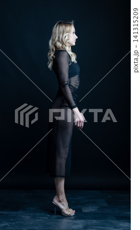 Young blonde dancer wearing transparent black dress and high heels posing in studio with black background Young blonde dancer wearing transparent black dress and high heels posing in studio with black background 141315209