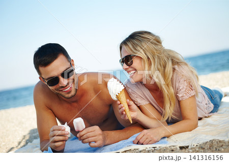 Couple, ice cream and beach for relax and travel outdoor for relationship and dating. Boyfriend, girlfriend or tourist with gelato dessert and smile by ocean for rest on towel in summer for holiday Couple, ice cream and beach for relax and travel outdoor for relationship and dating. Boyfriend, girlfriend or tourist with gelato dessert and smile by ocean for rest on towel in summer for holiday 141316156