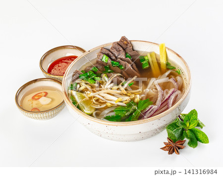 Bowl of pho bo with beef slices, rice noodles, herbs, bean sprouts, lime, and condiments on white background Bowl of pho bo with beef slices, rice noodles, herbs, bean sprouts, lime, and condiments on white background 141316984