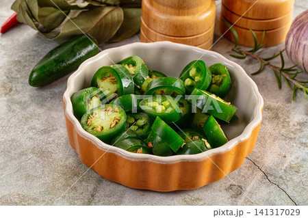 Sliced jalapeno peppers in ceramic bowl with kitchen herbs and wooden spice grinders Sliced jalapeno peppers in ceramic bowl with kitchen herbs and wooden spice grinders 141317029