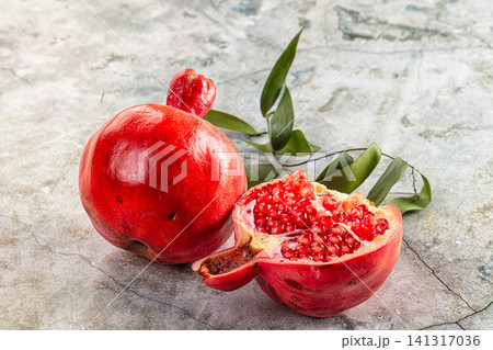 Fresh pomegranate fruit whole and sliced with green leaves on stone surface Fresh pomegranate fruit whole and sliced with green leaves on stone surface 141317036