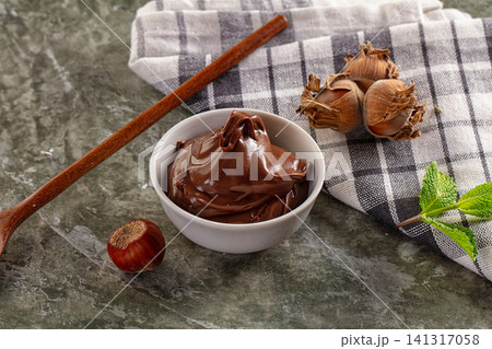 Rich chocolate spread in white bowl with hazelnuts and mint on marble surface Rich chocolate spread in white bowl with hazelnuts and mint on marble surface 141317058