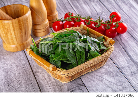 Fresh spinach in wicker basket with cherry tomatoes and wooden kitchen tools on rustic table 141317066