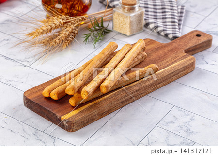 Breadsticks on wooden cutting board with wheat and herbs 141317121