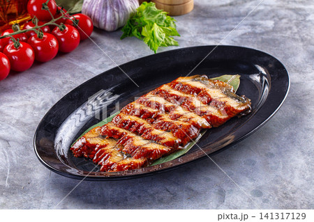 Grilled eel on black plate with cherry tomatoes and garlic Grilled eel on black plate with cherry tomatoes and garlic 141317129