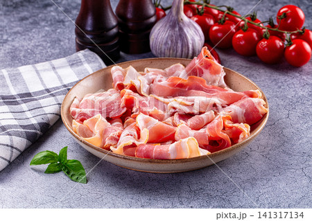 Sliced prosciutto in ceramic bowl with cherry tomatoes garlic and basil on gray surface Sliced prosciutto in ceramic bowl with cherry tomatoes garlic and basil on gray surface 141317134