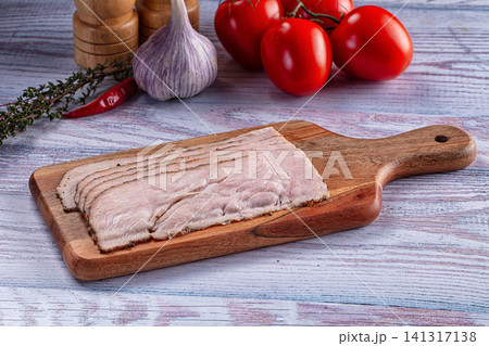 Sliced pastrami on wooden cutting board with fresh tomatoes garlic and herbs Sliced pastrami on wooden cutting board with fresh tomatoes garlic and herbs 141317138